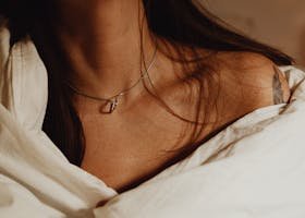 Close-up of a woman's collarbone with a necklace and tattoo, wrapped in fabric.